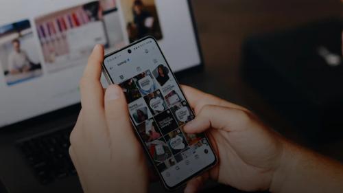 A person holding a cell phone in front of a laptop