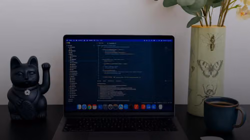 Laptop displaying code next to a lucky cat statue