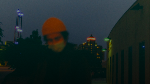 man in black jacket and orange knit cap standing on sidewalk during night time