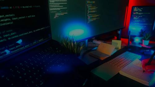 Computer screens displaying code with neon lighting.