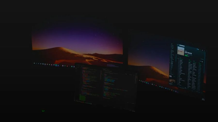 Three computer monitors displaying code and music software in a dark room