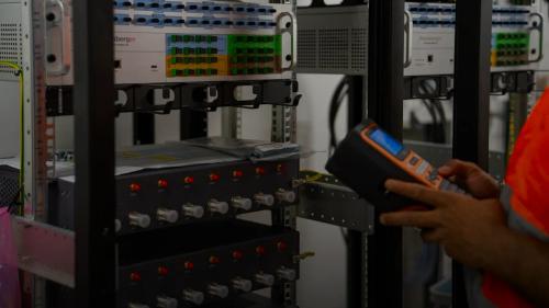 Technician inspecting server racks with a handheld diagnostic tool.
