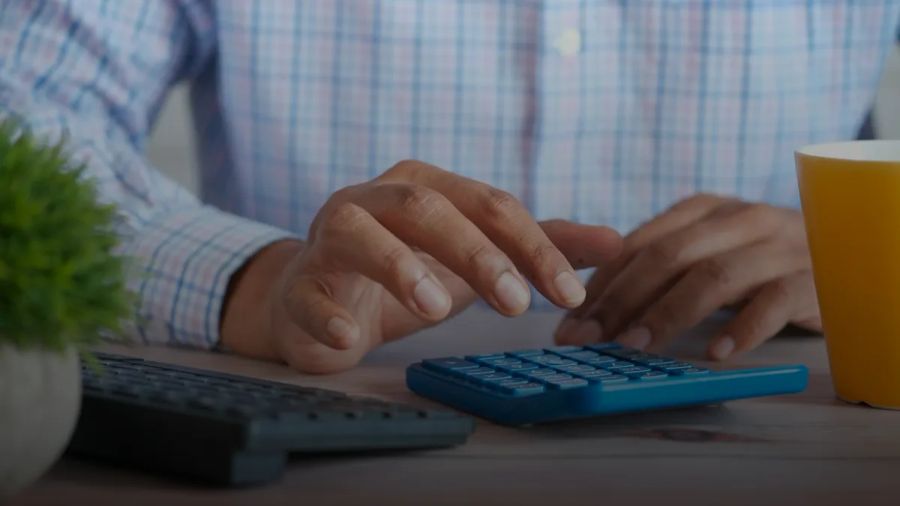person using calculator at desk with coffee mug