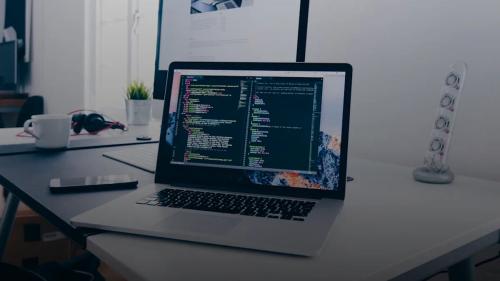 A MacBook with lines of code on its screen on a busy desk