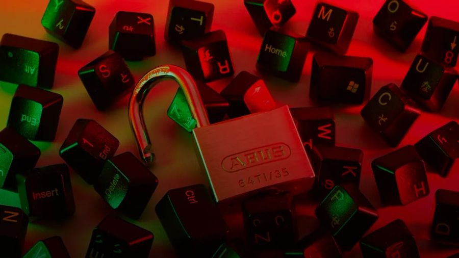 An open padlock surrounded by scattered black computer keyboard keys under red and green light