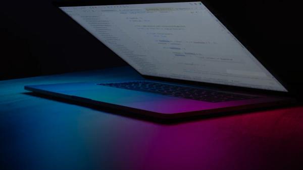 Open laptop with code on screen, neon lighting