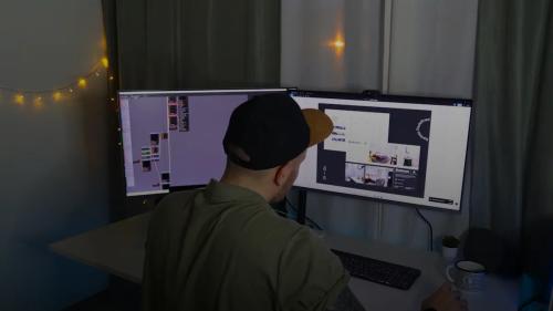 man in green dress shirt and black cap sitting in front of computer